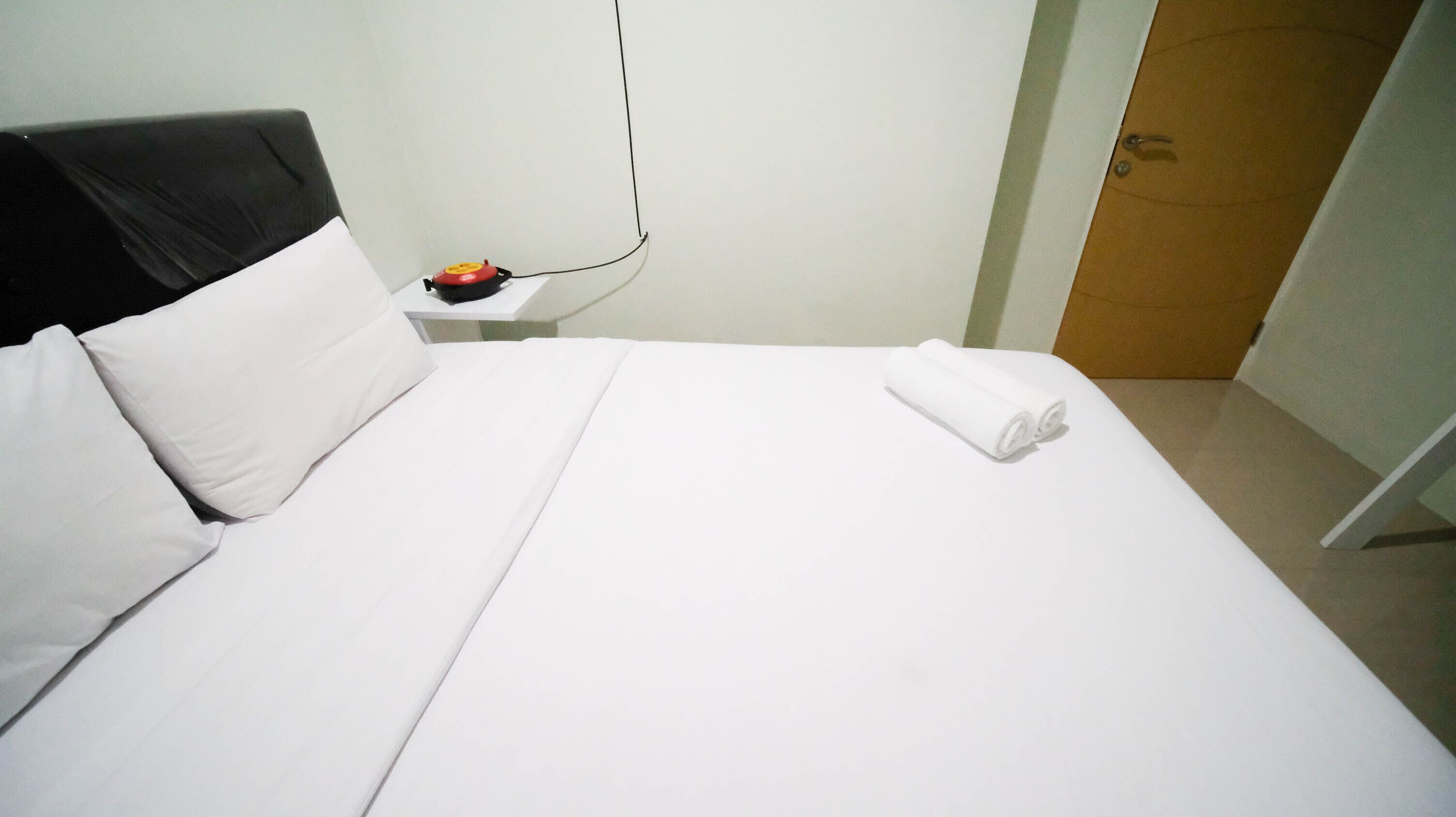 A neatly made bed with white linens, a black headboard, and a rolled white towel on the footboard.