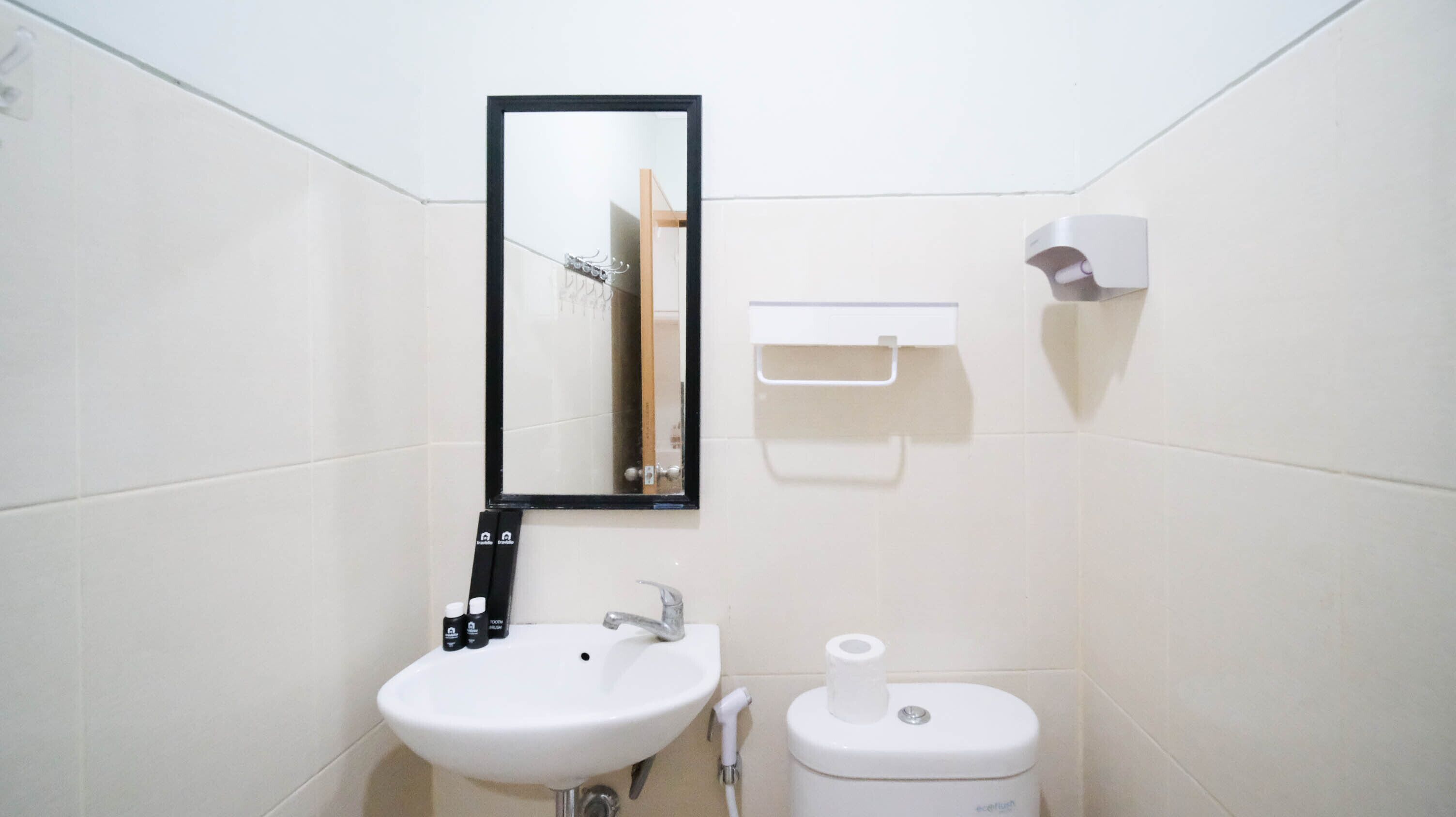 A small, clean bathroom with a white sink, a mirror, a toilet, and a soap dispenser.