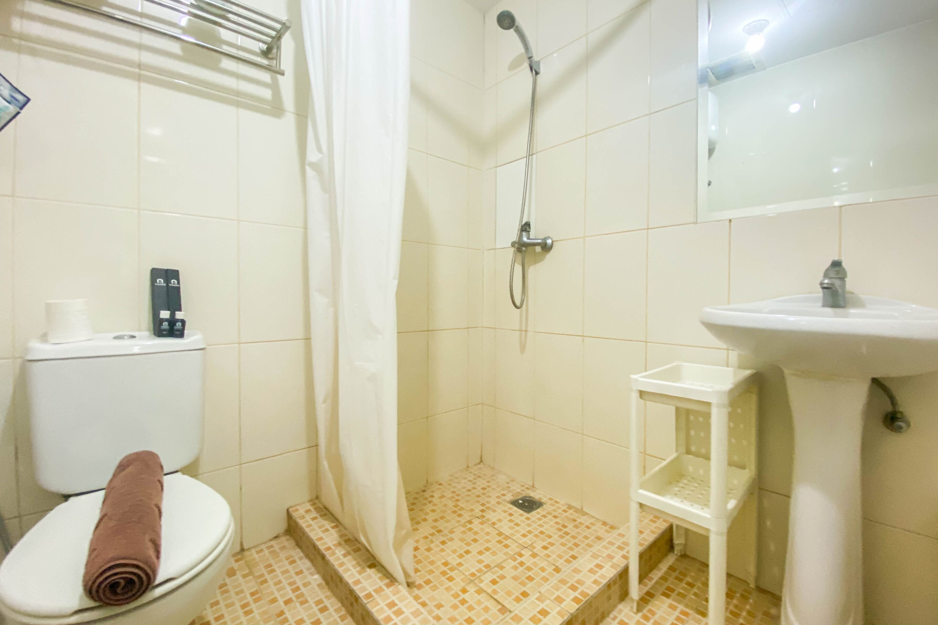 Un baño con inodoro, ducha, lavamanos y un pequeño estante blanco.