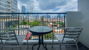 A balcony with a round glass table and two chairs, overlooking a cityscape with various buildings and a cloudy sky. - Cozy Stay Studio At Ambassade Kuningan Apartment (Jakarta)