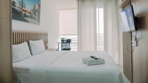 Ein Hotelzimmer mit einem Bett, einem Fernseher, einem Fenster mit Vorhängen und einem Bild an der Wand.