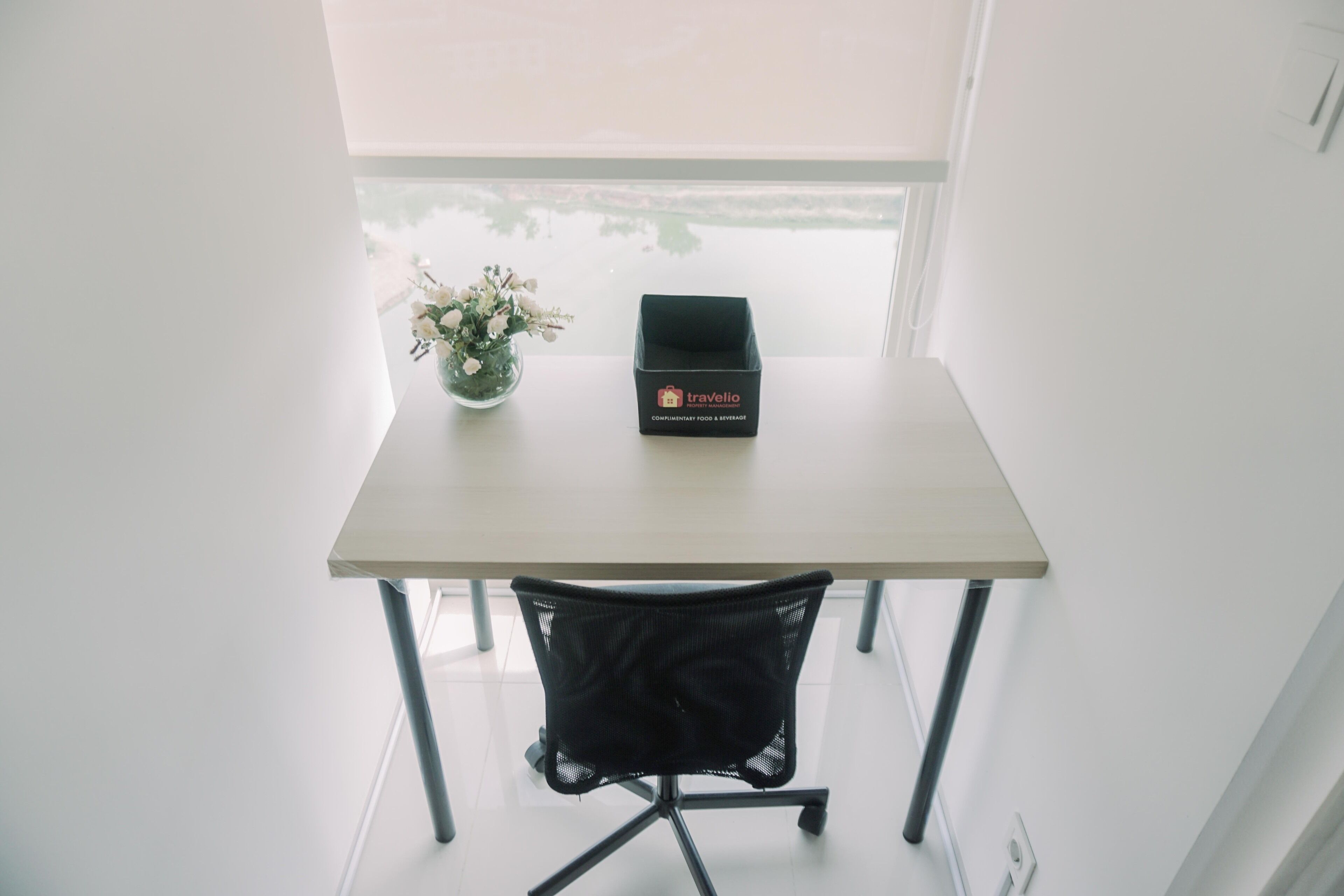 A small table with a black box labeled 'Travelio' and a vase with flowers.