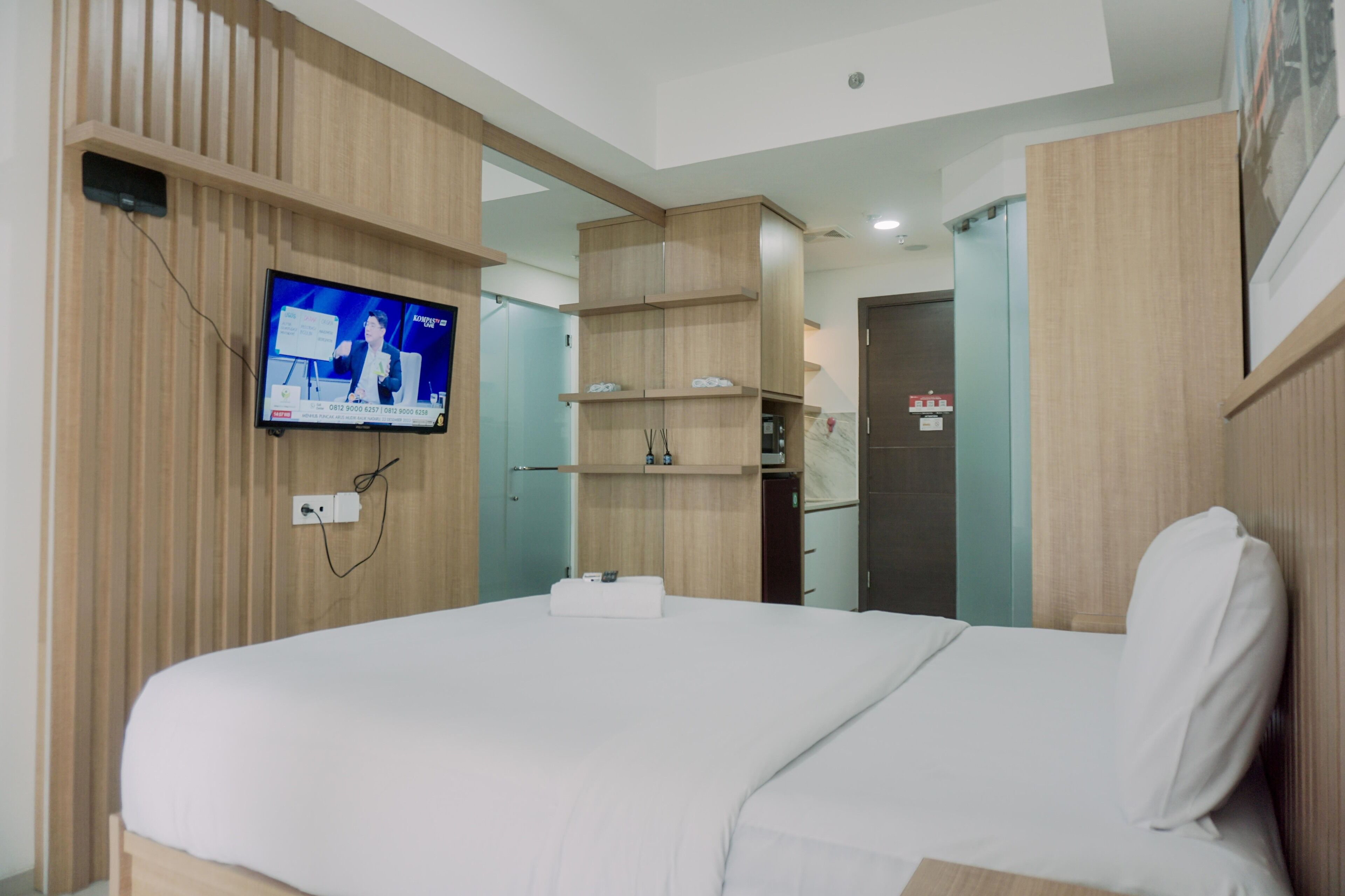 Une chambre d’hôtel moderne dotée d’un grand lit, de lambris en bois, d’un téléviseur fixé au mur et d’étagères intégrées.