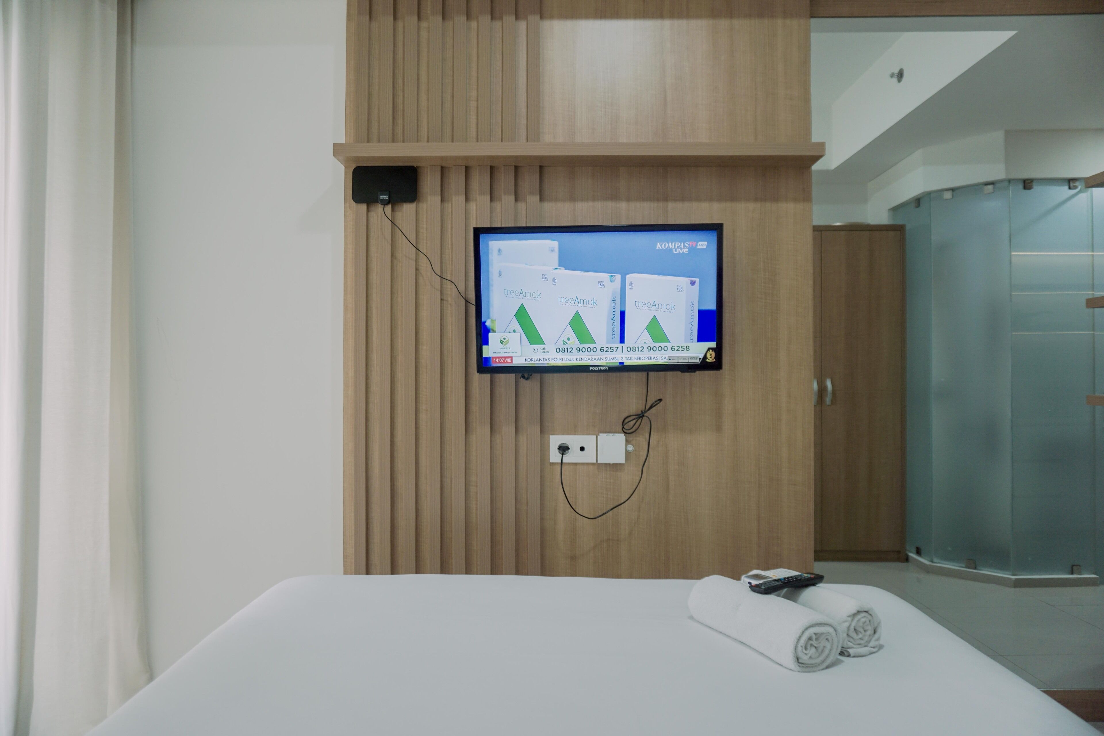 A hotel room with a bed, a TV mounted on the wall, and a shower area.