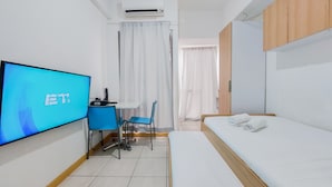 Quarto de hotel com cama, secretária e cadeira, televisão e aparelho de ar condicionado.