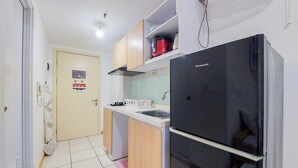 Uma cozinha compacta com geladeira preta, armários de madeira e bancada branca.