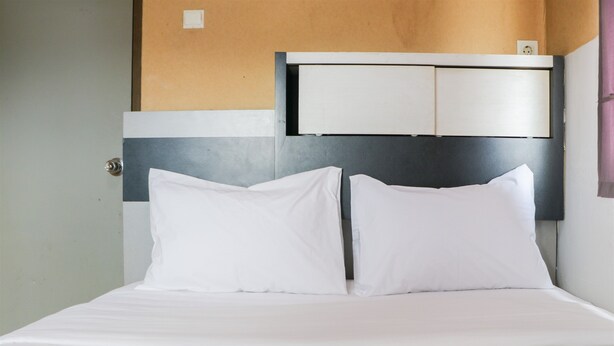 Una cama con ropa blanca, un cabecero con espacio de almacenamiento y una puerta a la izquierda.