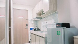 A compact kitchen with a refrigerator, a kettle, and a sink.