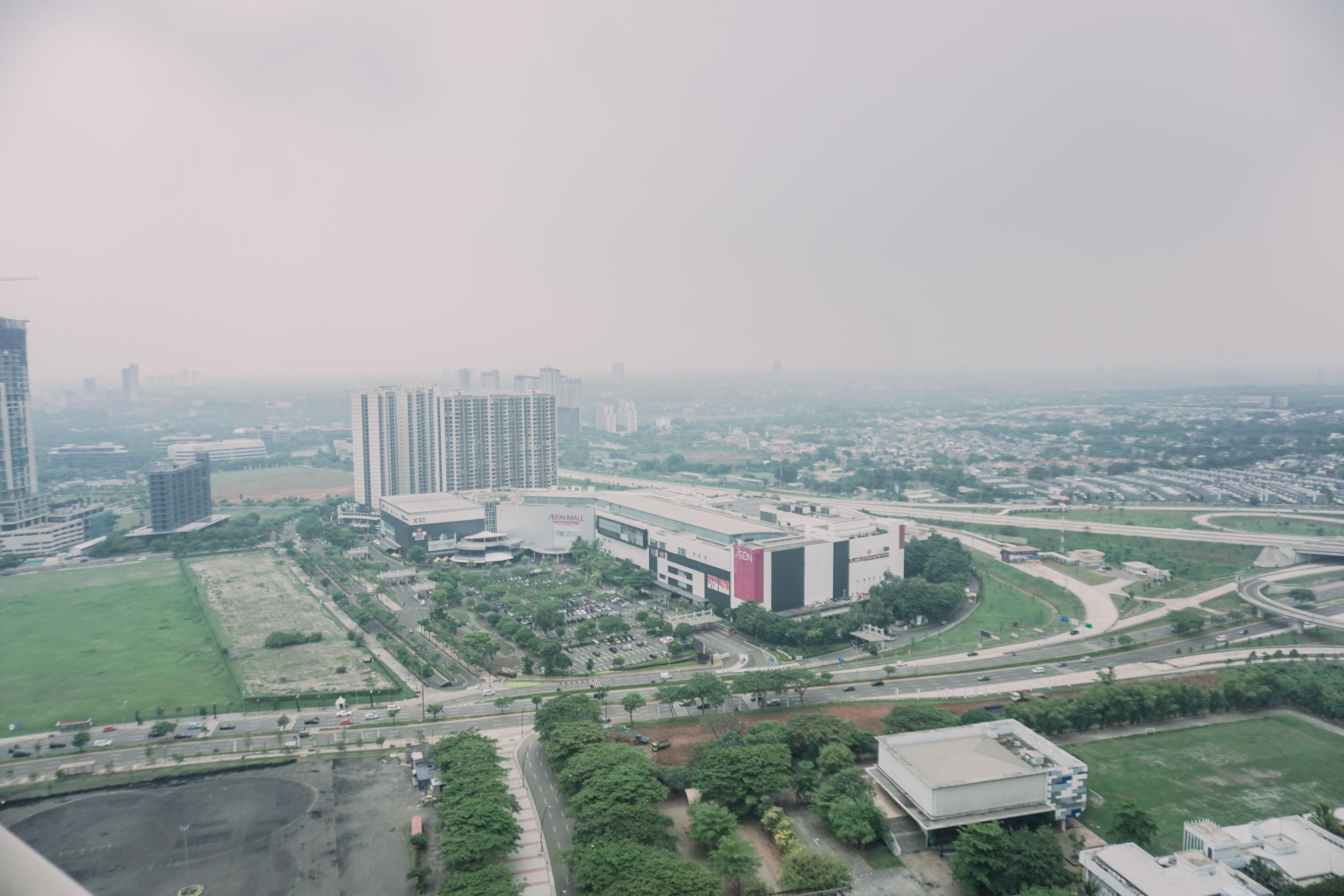 Vista aérea de un paisaje urbano con rascacielos, un gran complejo comercial y zonas verdes circundantes.