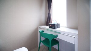 A small room with a desk, a green chair, a window with curtains, and a box labeled "travelio" on the desk. - Modern And Homey Studio At Tanglin Supermall Mansion Apartment (Surabaya)