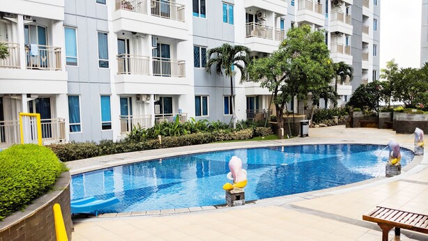 A swimming pool surrounded by a landscaped area with a multi-story residential building in the background. - Modern And Homey Studio At Tanglin Supermall Mansion Apartment (Surabaya)
