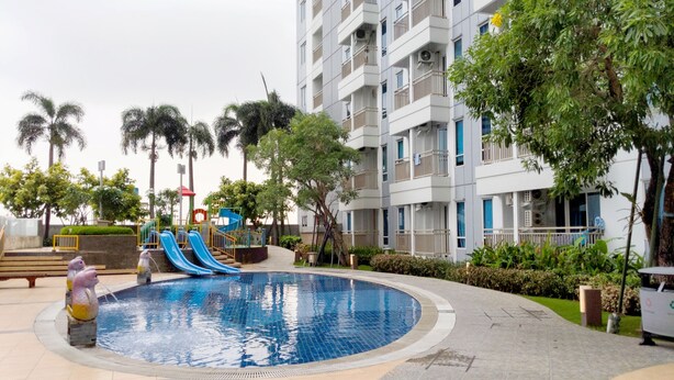 A swimming pool with a slide, surrounded by palm trees and a multi-story building. - Simple And Cozy Studio At Tanglin Supermall Mansion Apartment (Surabaya)