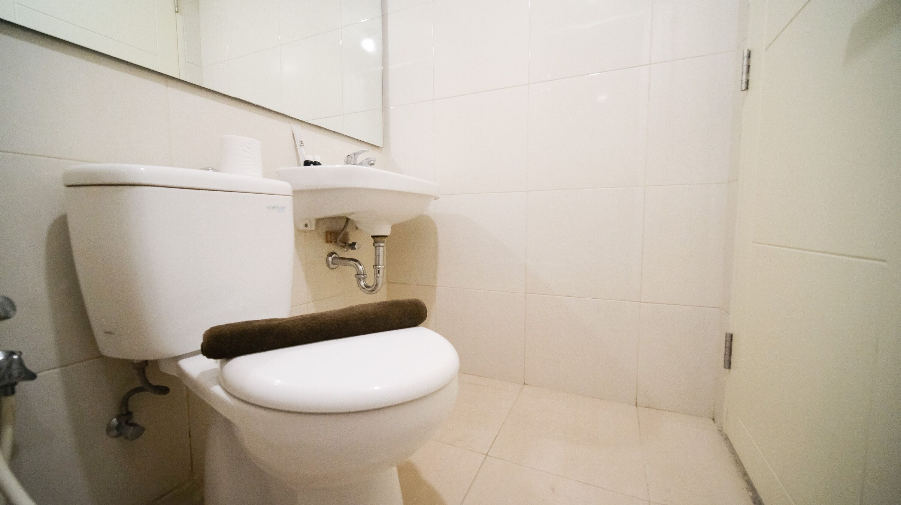 Et standard toilet med et brunt gulvtæppe, en hvid vask og et spejl over vasken.