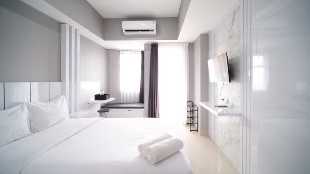 Une chambre d’hôtel moderne dotée d’un grand lit, d’un téléviseur à écran plat, d’un bureau et d’une salle de bain visible à travers une fenêtre.