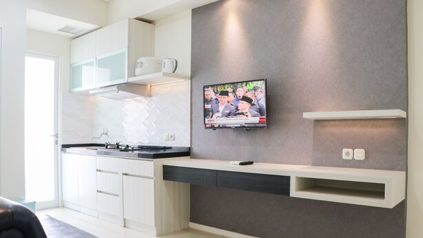 A modern kitchen with white cabinets, a built-in stove, and a flat-screen TV mounted on the wall. - Simply 2Br Apartment At Parahyangan Residence (Bandung)