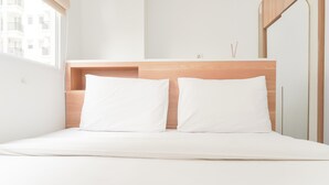A minimalist bedroom with a wooden headboard, two white pillows, and a bedside table with a lamp. - Good Choice And Homey 2Br At Signature Park Grande Apartment (Jakarta)