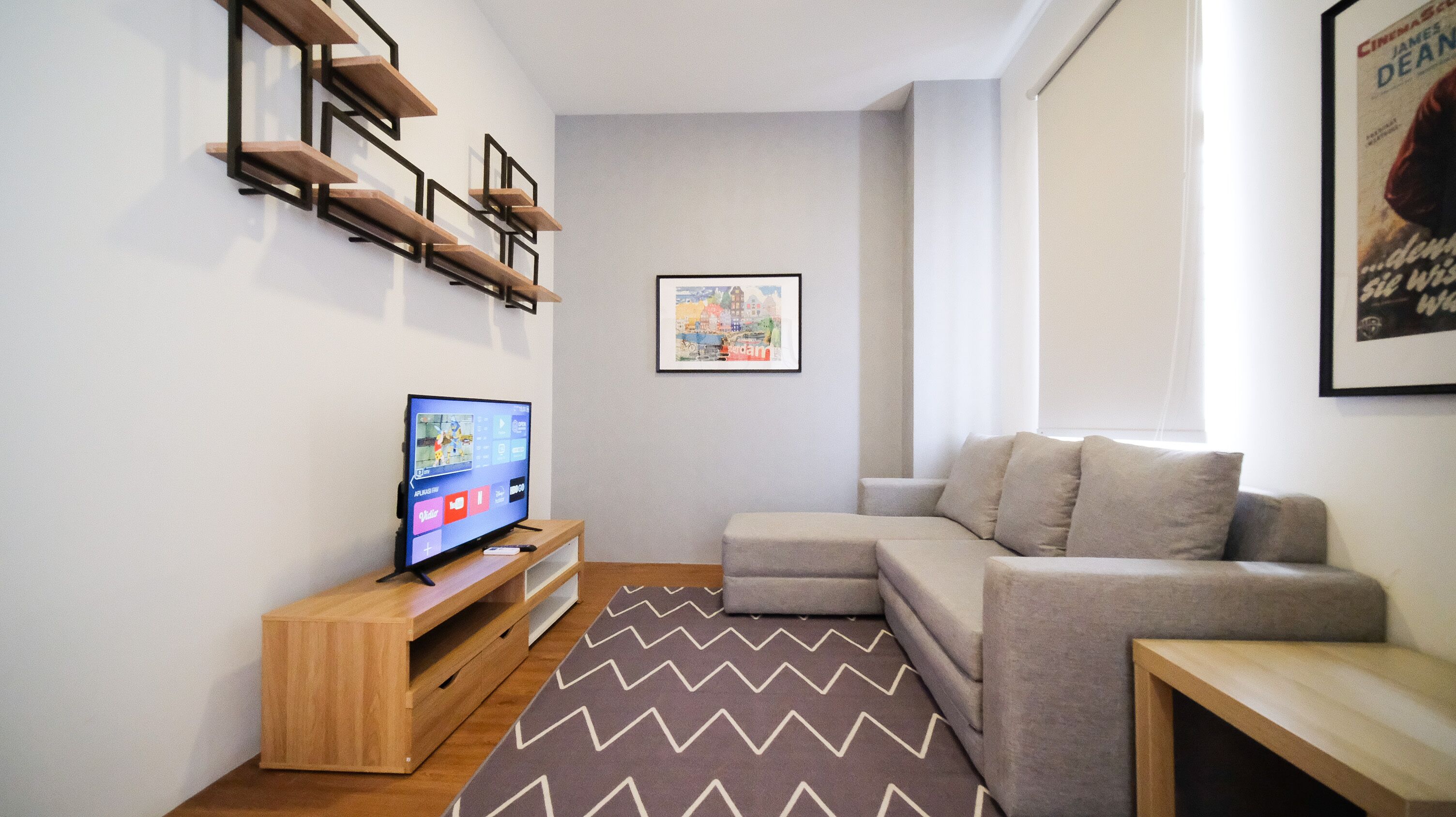 Una sala de estar moderna con un televisor sobre un mueble de madera, un sofá gris y una alfombra estampada.
