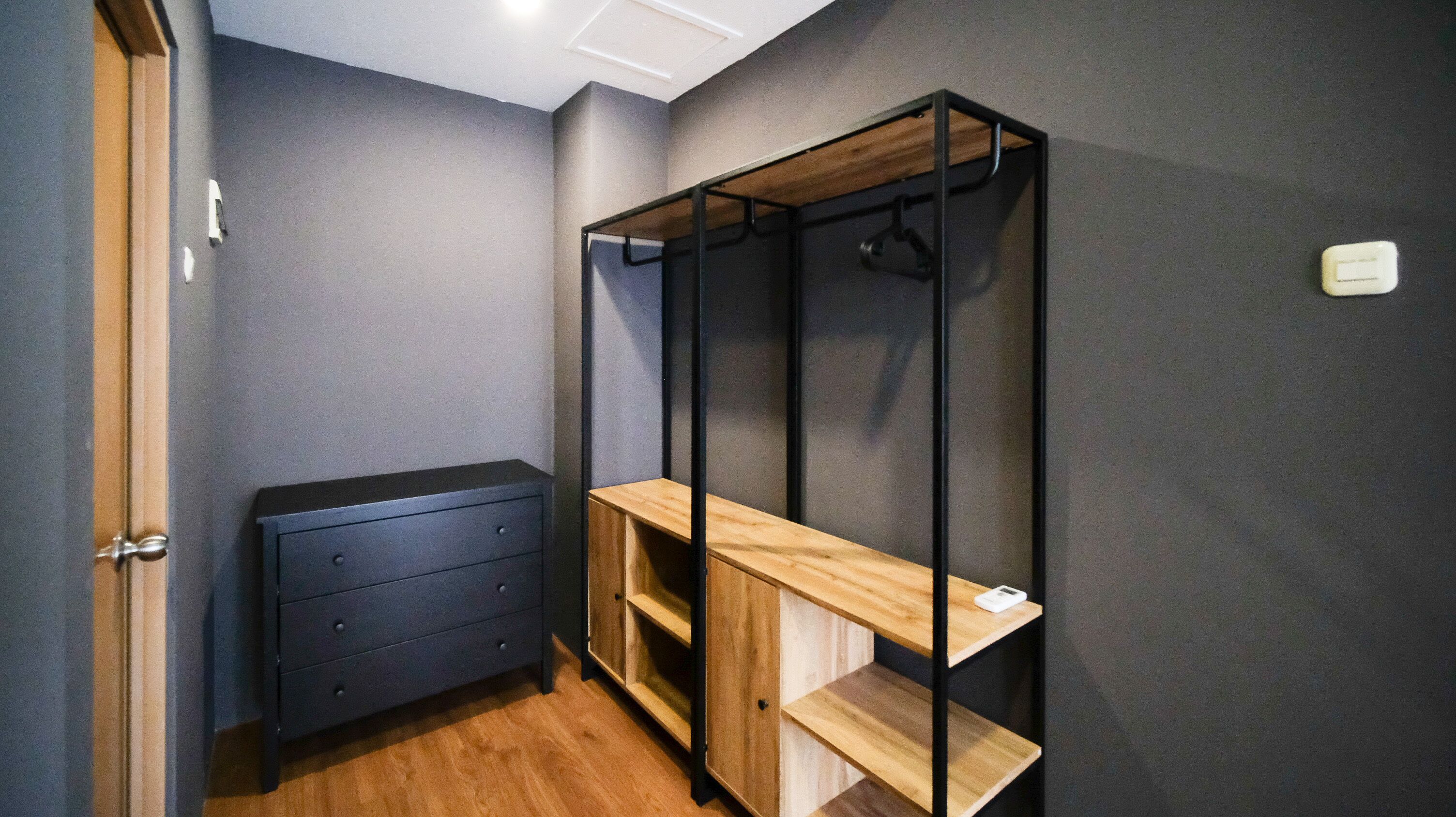 Une pièce de taille modeste, avec une commode bleu foncé, un banc en bois doté d’étagères et une armoire en métal.