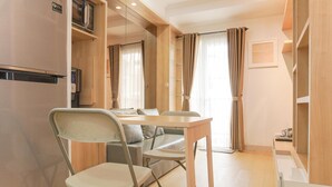 A compact living space with a dining area, a foldable chair, a small table, a refrigerator, and a microwave. - Nice And Homey 2Br Signature Park Grande Apartment (Jakarta)