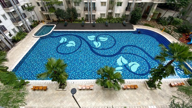 A large indoor swimming pool with a mosaic design, surrounded by palm trees and benches. - Nice And Homey 2Br Signature Park Grande Apartment (Jakarta)