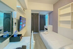 A modern hotel room with a bed, a desk with a computer, a TV, and a minibar.