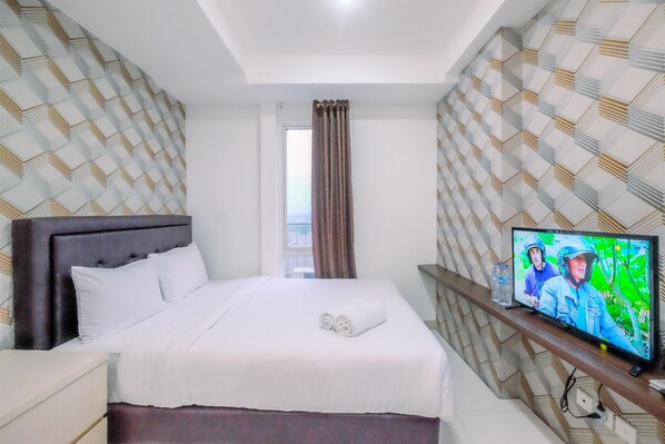 A hotel room with a large bed, a television, and patterned wallpaper.
