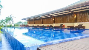A swimming pool with clear blue water, wooden deck, and lounge chairs. - Good Deal And Homey Studio Azalea Suites Apartment Cikarang (Cikarang)