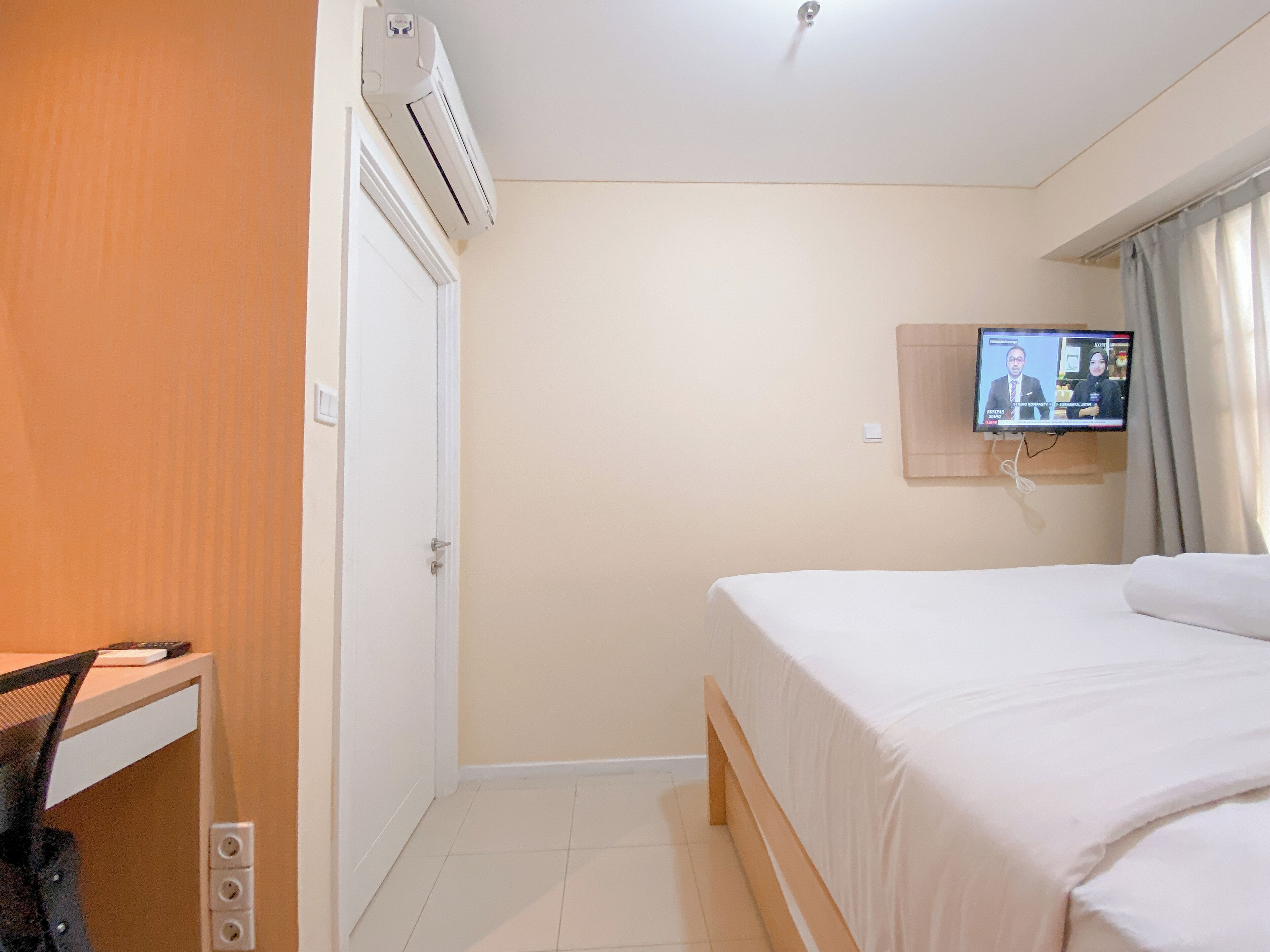 A hotel room with a bed, a desk, an air conditioning unit, a television, and a door.