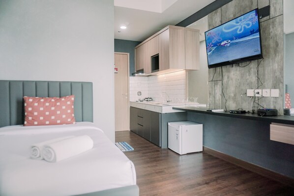 A modern hotel room with a bed, a small kitchenette, and a TV mounted on the wall. - Simply And Cozy Stay Studio Apartment B Residence (Pagedangan)