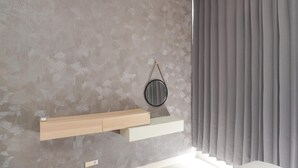 Ein Zimmer mit einer strukturierten grauen Wand, einem Holzregal, einem weißen Regal und einem Fenster mit grauen Vorhängen.