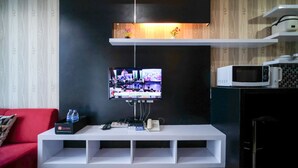Una sala de estar moderna con un televisor de pantalla plana montado sobre un mueble blanco, un sofá rojo y un microondas en un gabinete.
