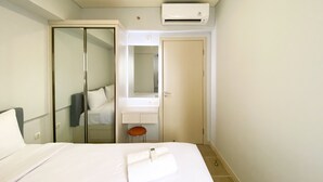 A hotel room with a bed, a mirror, a wardrobe, a bathroom, and an air conditioning unit. - Best Deal And Cozy 3Br Meikarta Apartment (Cikarang)