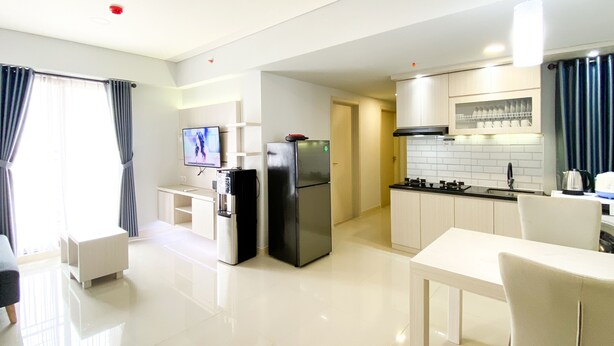 A modern kitchen with a refrigerator, stove, and sink. There is a dining area with a table and chairs. - Best Deal And Cozy 3Br Meikarta Apartment (Cikarang)