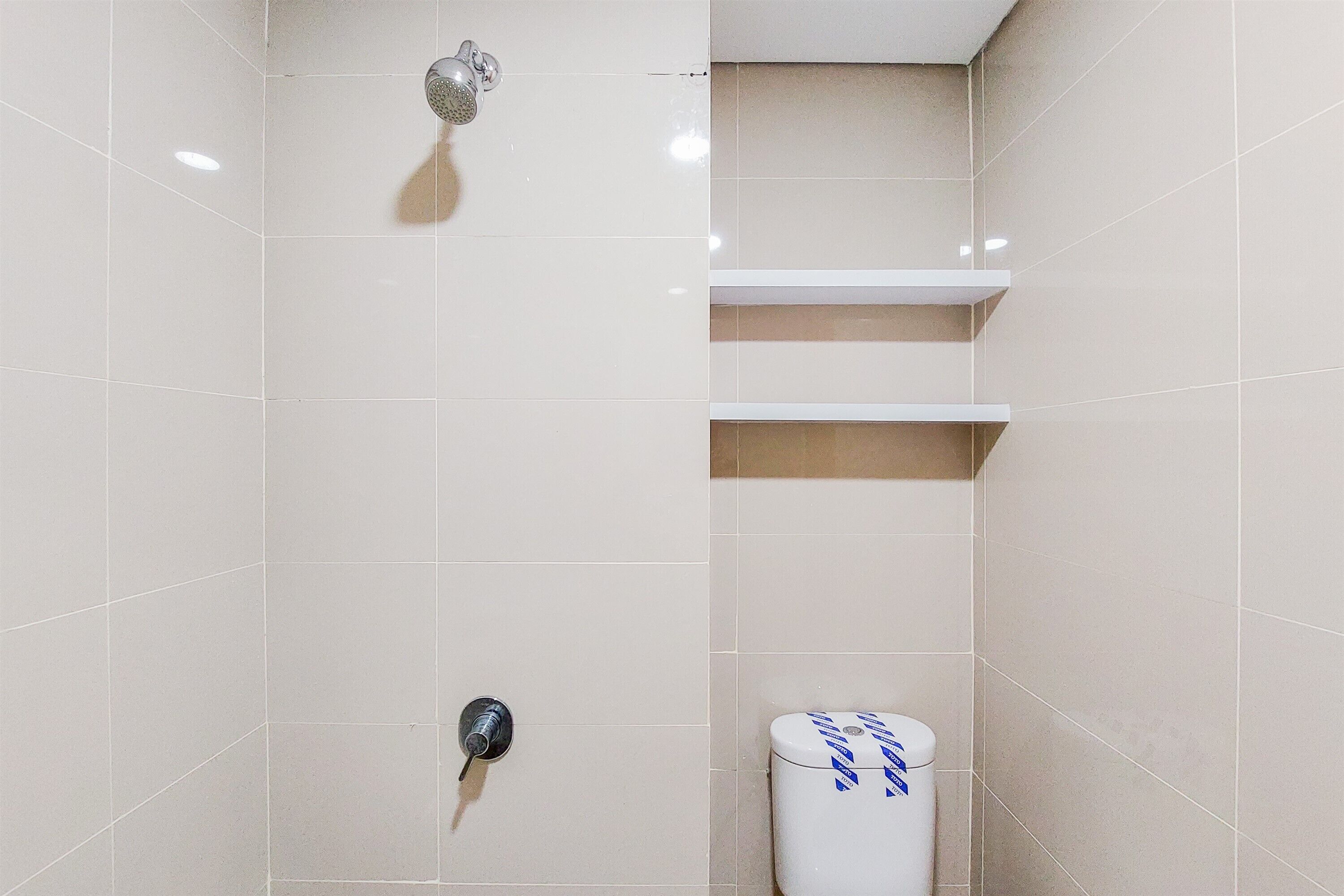 A bathroom with beige tiles, a showerhead, a toilet, and a shelf.