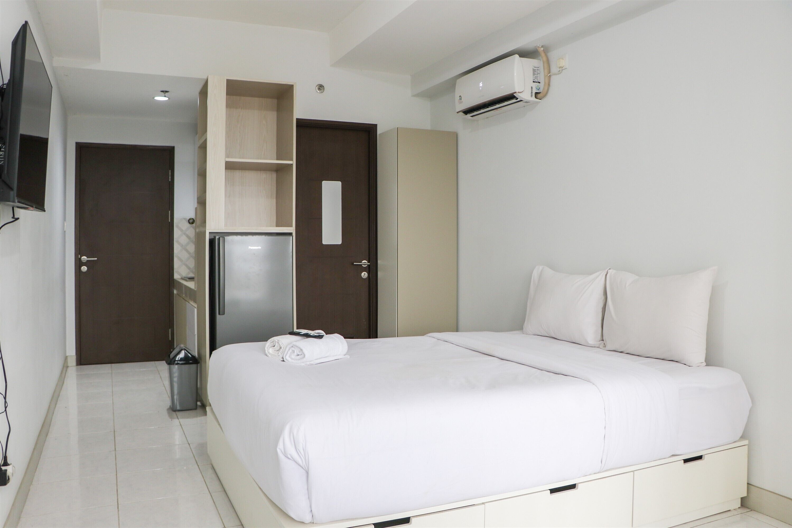 Une chambre d’hôtel équipée d’un lit, d’une armoire, d’un petit réfrigérateur, d’une poubelle et d’un appareil de climatisation.