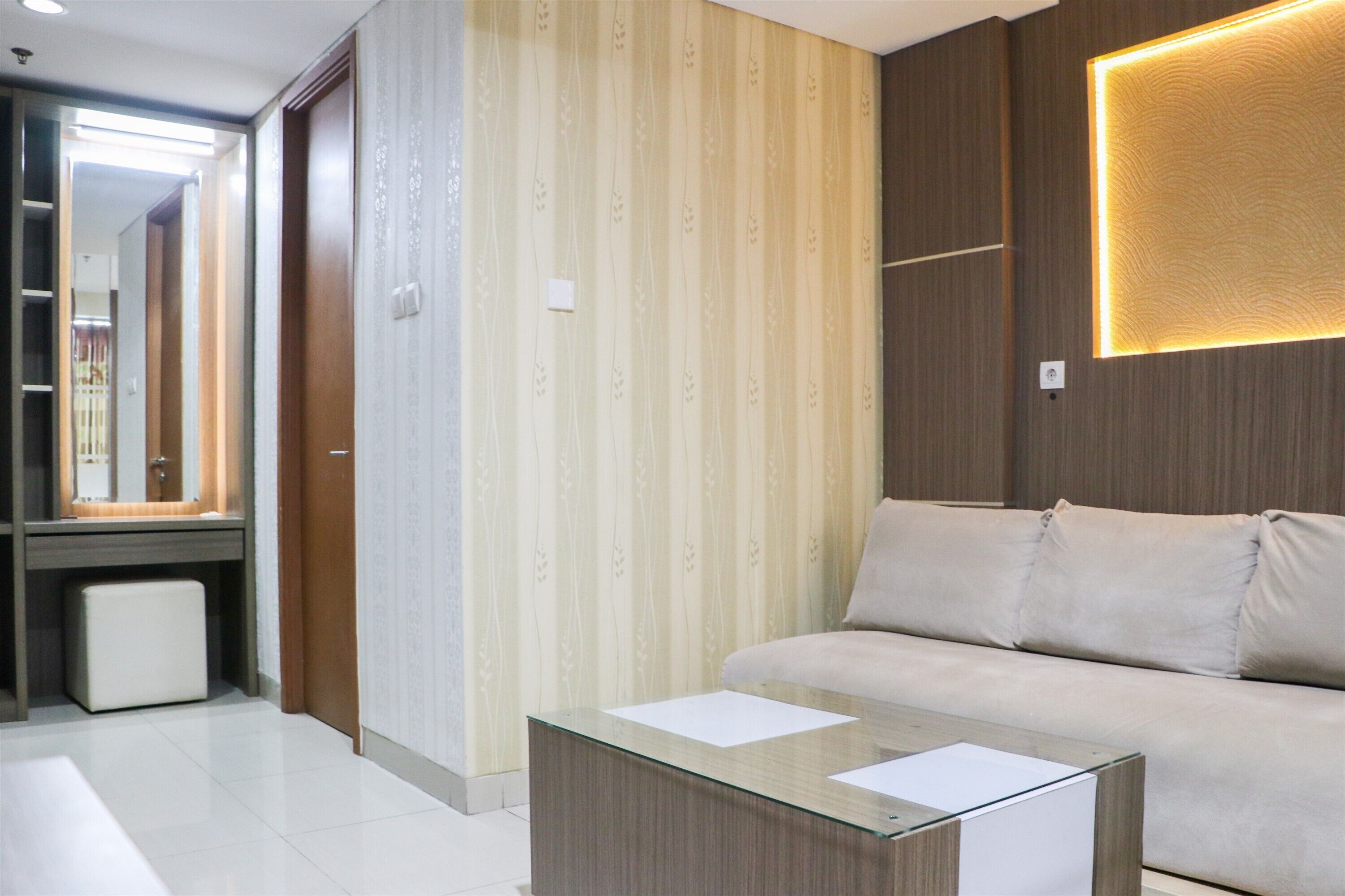 A modern hotel room with a sofa, a glass coffee table, a mirror, and a patterned wallpaper.