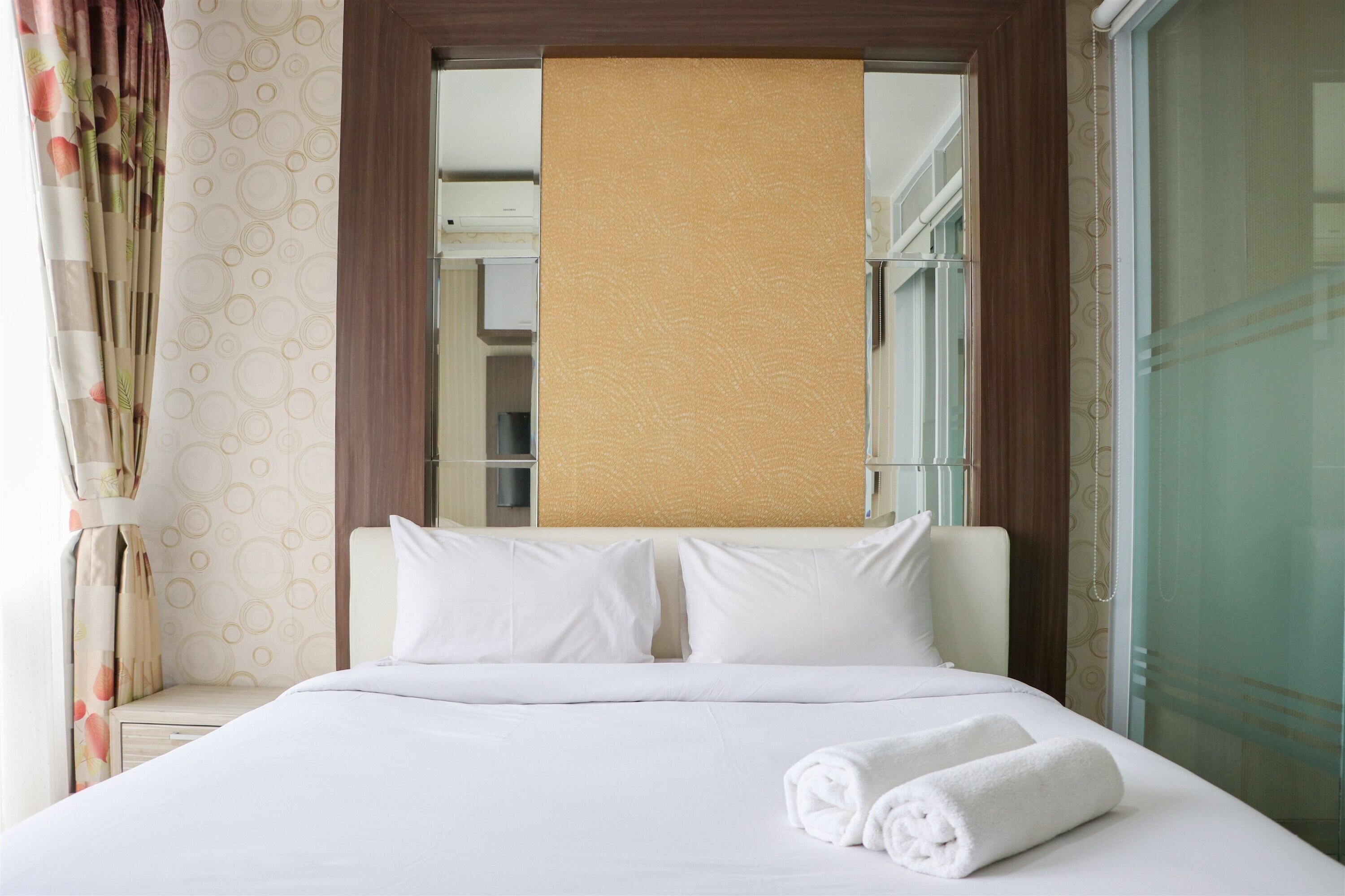 A hotel room with a bed, white linens, a rolled towel, and a window with curtains.