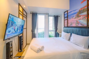 A hotel room with a large bed, a flat-screen TV mounted on the wall, a view of the outdoors through a window, and a decorative wall mural. - Homey And Relaxing Studio Tokyo Riverside Pik 2 Apartment (Teluknaga)