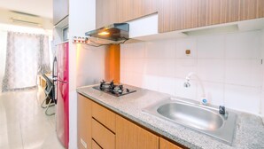 A kitchen with a stainless steel sink, a gas stove, wooden cabinets, and a window with curtains. - Good Deal And Homey Studio At Park View Condominium (Depok)