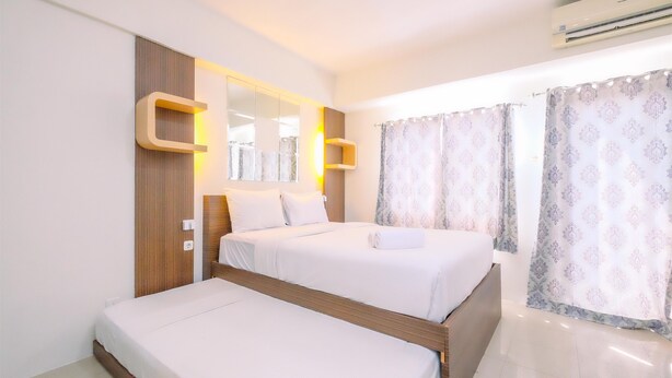 A hotel room with two beds, a large mirror, a built-in shelf, and a window with patterned curtains. - Good Deal And Homey Studio At Park View Condominium (Depok)