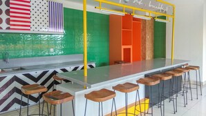 A modern kitchen with a bar area, green and orange tiled walls, and a yellow overhead bar. - Enjoy Living And Homey Studio Dave Apartment (Depok)
