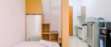 A compact hotel room with a bed, a kitchenette, and a small bathroom.