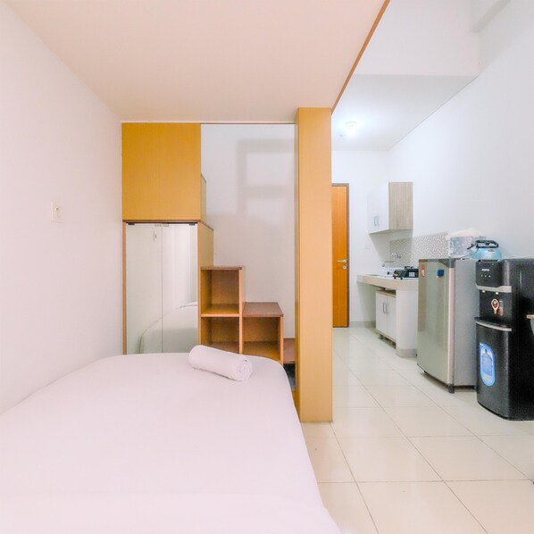 A compact hotel room with a bed, a kitchenette, and a small bathroom. - Enjoy Living And Homey Studio Dave Apartment (Depok)