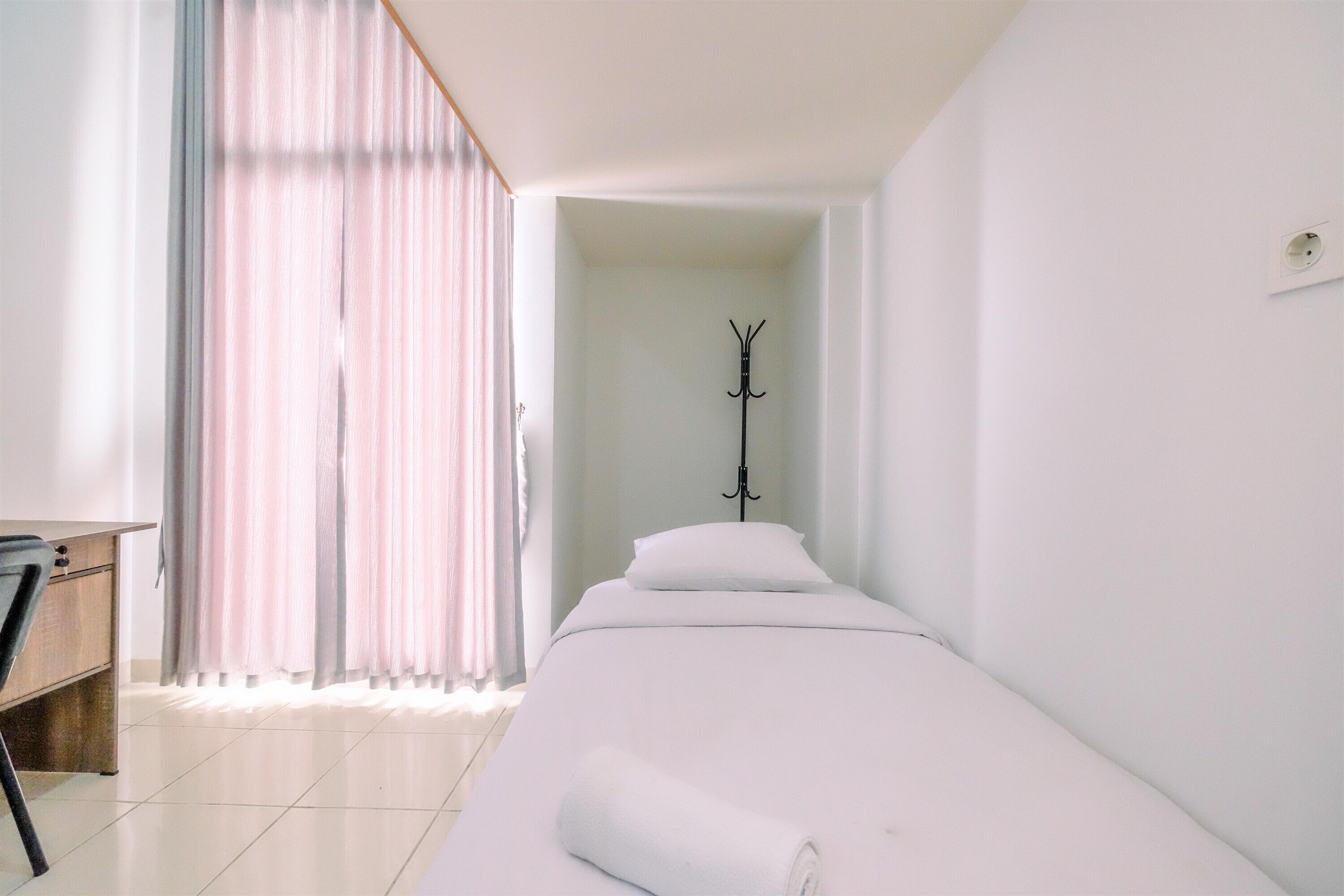 A hotel room with a bed, a desk, and a coat rack.