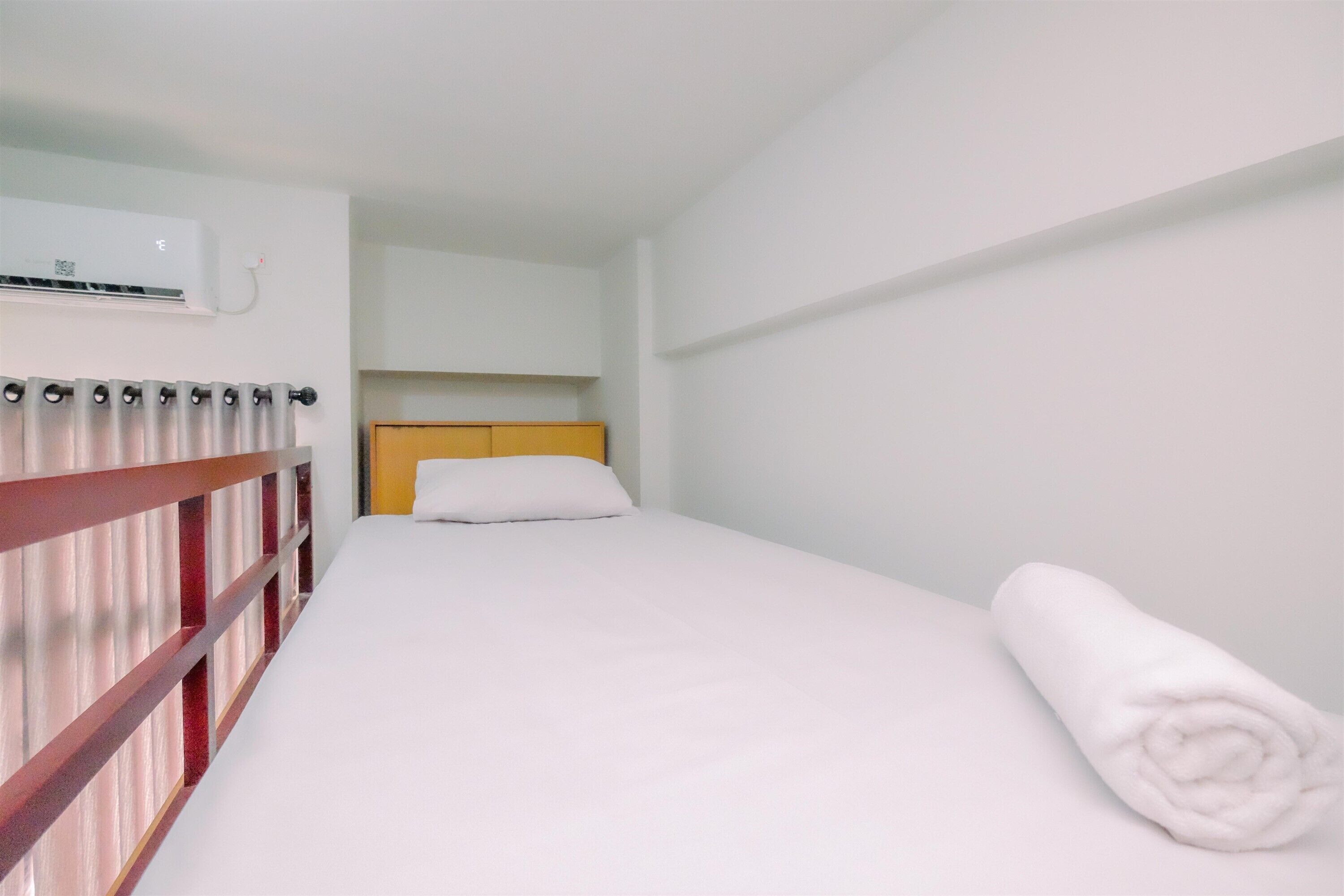 Ein Einzelbett mit weißer Bettwäsche, einem Holz-Kopfteil und einer weißen Wand.
