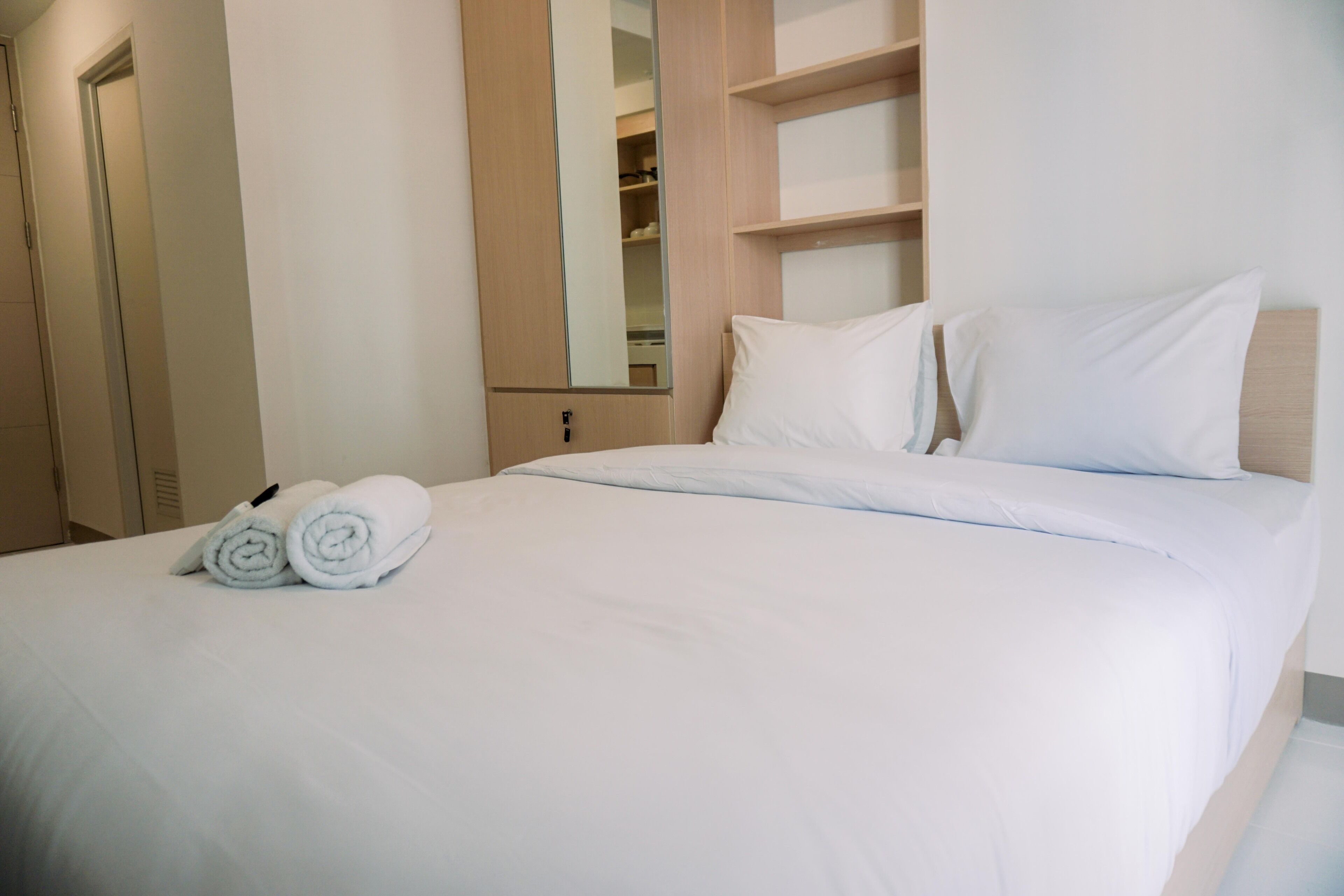 A neatly made bed with white linens and two rolled towels placed at the foot of the bed.