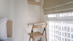 A room with a bed, a wooden chair, a shelf, and a window with a view of buildings. - Relax And Comfy Studio At Tokyo Riverside Pik 2 Apartment (Teluknaga)