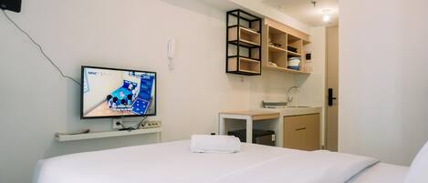 A hotel room with a bed, a TV mounted on the wall, a small desk with a sink, and a shelf unit.