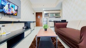 A modern living room with a flat-screen TV, a sofa, a coffee table, and a kitchen area in the background.