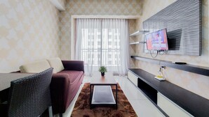 A modern living room with a sofa, a coffee table, a TV mounted on the wall, and a window with sheer curtains.
